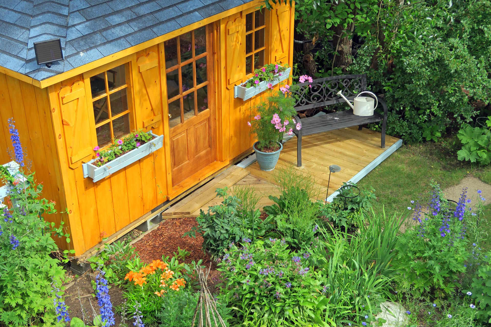 Gartenhaus aus Holz mit Sprossenfenstern und Blumenkasten in einem bepflanzten Garten