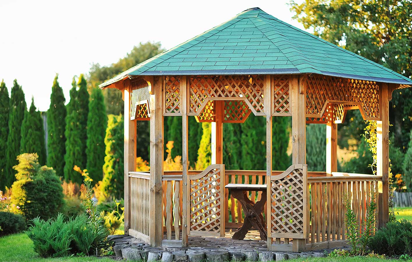 Mehreckiger Holzpavillon mit grünem Dach und Rankgitter-Wänden als überdachter Sitzplatz im Garten