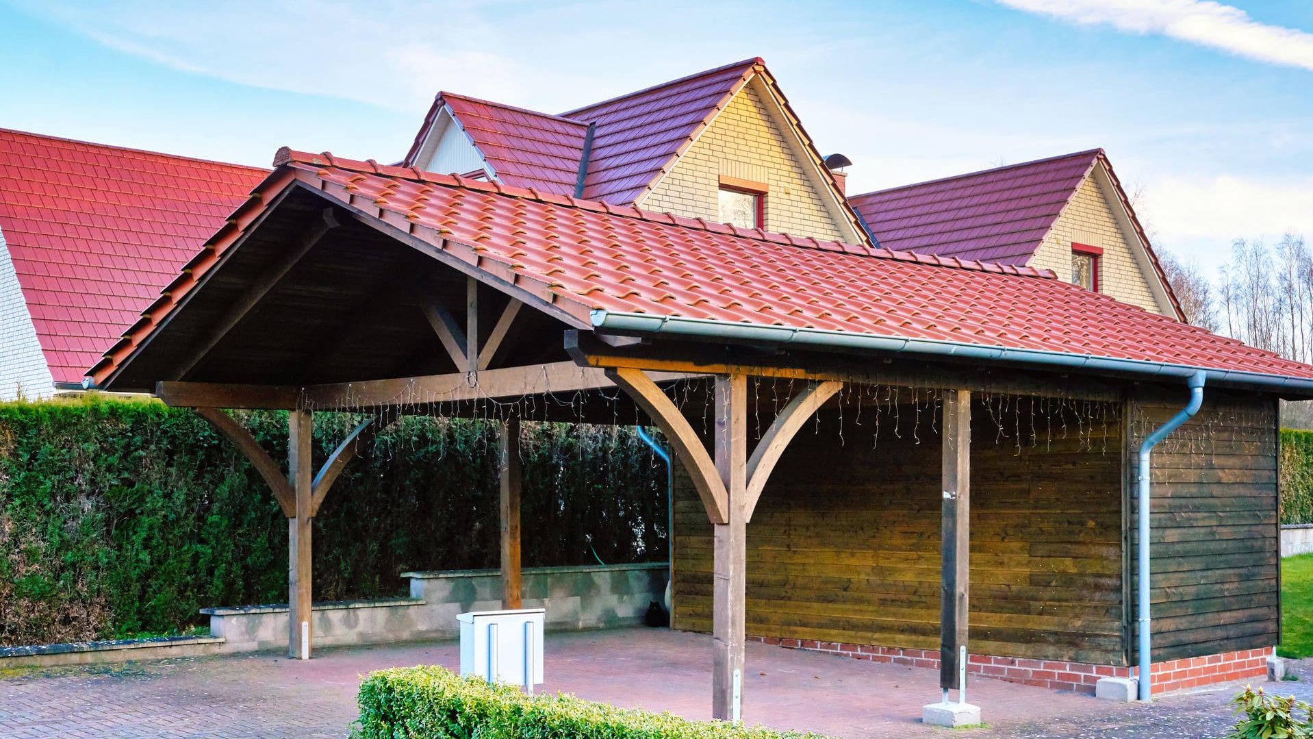 Carport aus Holz mit Dach neben einem Wohnhaus